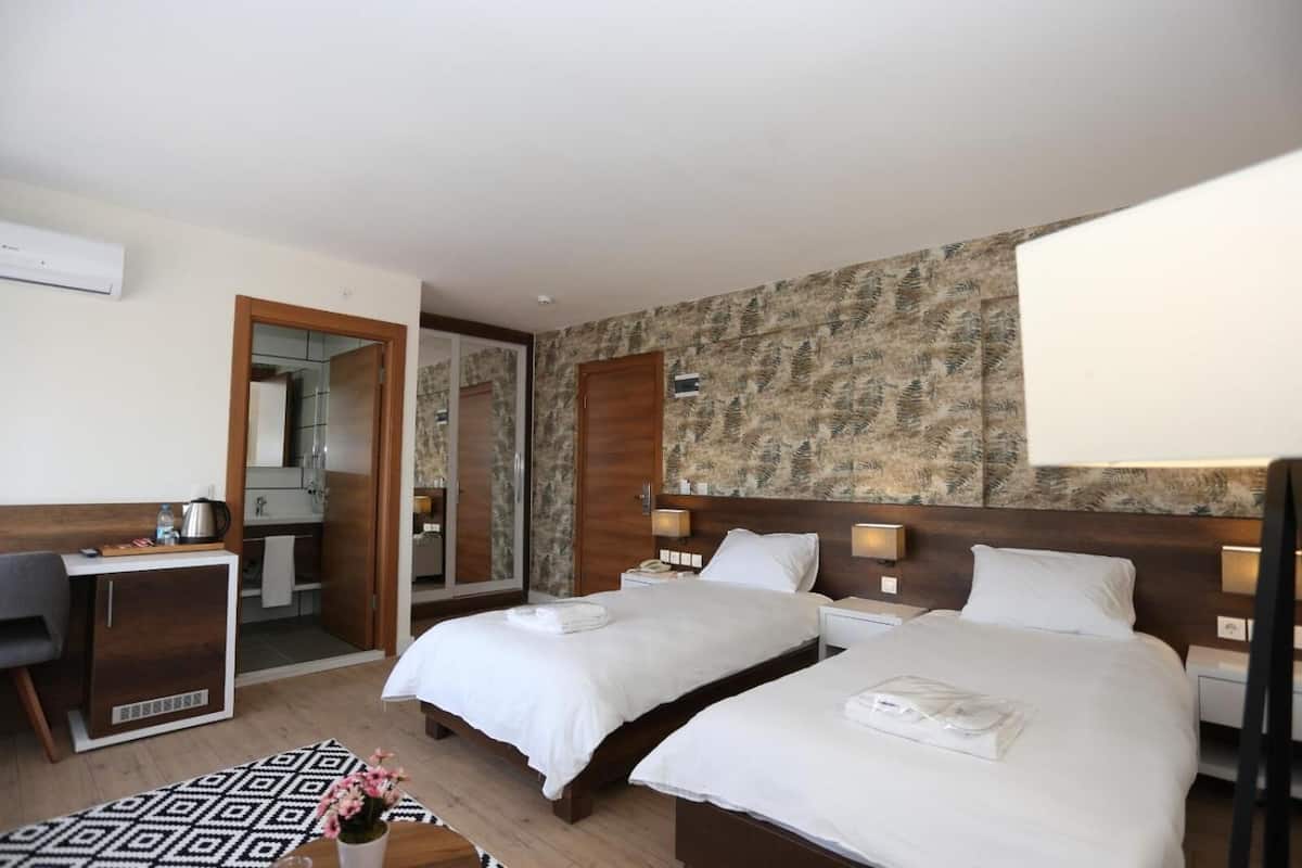 A hotel room with two beds, a desk, a chair, a mirror, and a patterned wall.
