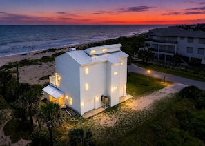 A white building with multiple windows and a balcony, located near a beach with a view of the ocean.
