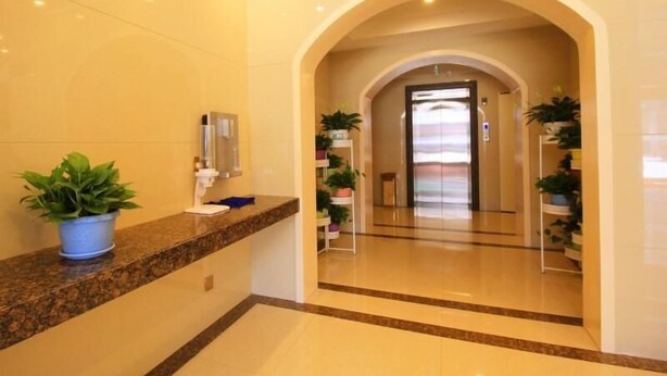 A hotel lobby with a marble reception desk, potted plants, and a glass elevator. - Greentree Inn Xinzhou Jianshe Road Express Hotel (Xinzhou)