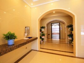 Un vestíbulo de hotel con mostrador de recepción de mármol, plantas en macetas y un ascensor de vidrio.