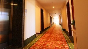 A hotel corridor with a carpeted floor, doors on both sides, and an elevator on the left. - Greentree Inn Xinzhou Jianshe Road Express Hotel (Xinzhou)