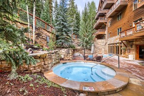 A stone-walled pool area with a hot tub, surrounded by trees and a wooden building. - 3059 The Timbers 2 Bedroom Condo by RedAwning (Keystone)