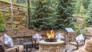 An outdoor patio with stone walls, a fire pit, and seating with patterned cushions. - 3059 The Timbers 2 Bedroom Condo by RedAwning (Keystone)