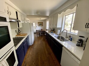 Una cocina con alacenas blancas, estufa, refrigerador, pileta y ventana.