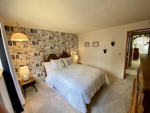 Un dormitorio con papel tapiz estampado, una cama con ropa de cama blanca, dos lámparas de noche y un armario de madera.