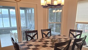 A dining room with a checkered tablecloth, wooden chairs, a chandelier, and large windows offering a view of a body of water. - Amazing! Tellico village lake house with dock! (Loudon)
