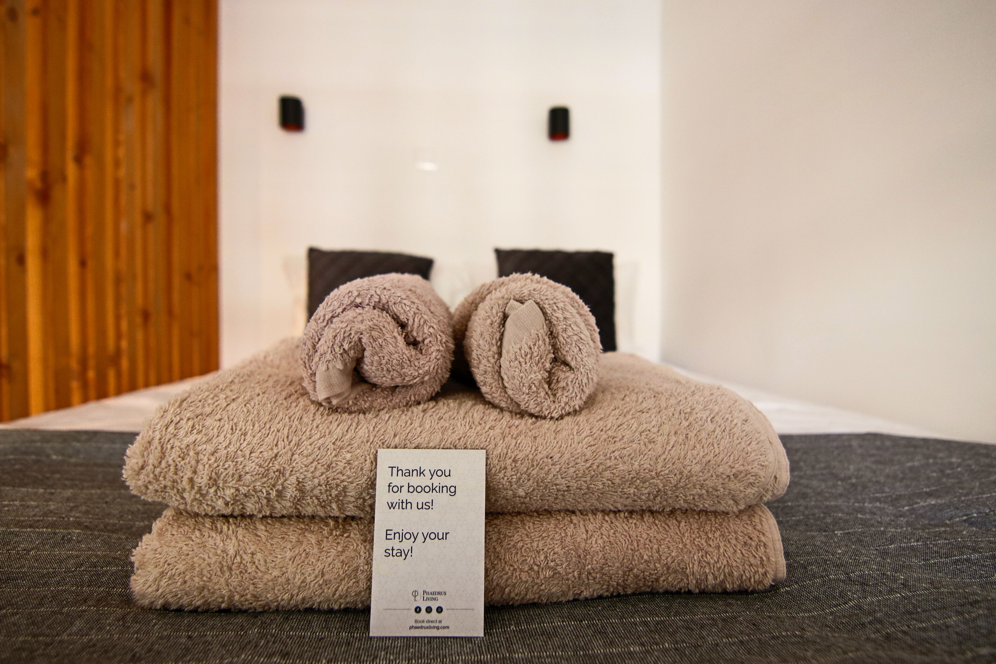 Een keurig opgevouwen, beige handdoek met een bedankkaartje op een bed.