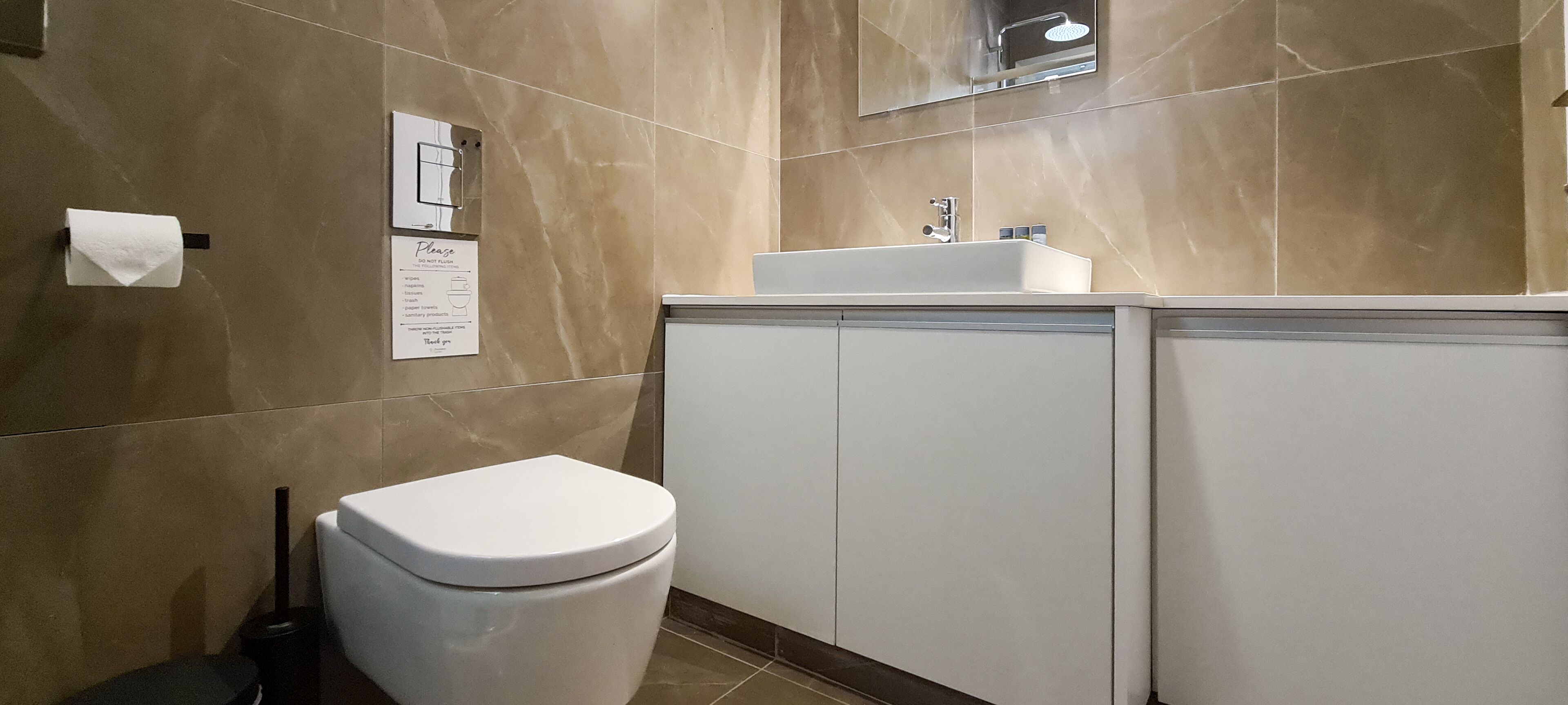 A bathroom with a white toilet, a sink, and cabinets. There is a sign on the wall and a mirror above the sink.