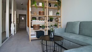 A modern living room with a grey sofa, a round black coffee table, and a wooden shelving unit with various decorative items and plants. - Phaedrus Living: Seaside Luxury Flat Athina 123 (Paphos)