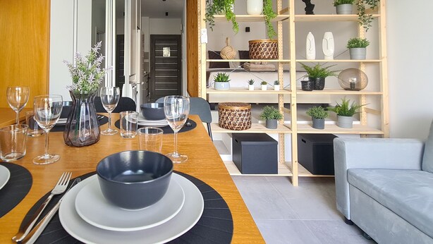 A dining area with a wooden table set for four, including plates, bowls, cutlery, and wine glasses. A television is mounted on the wall to the left. - Phaedrus Living: Seaside Luxury Flat Athina 123 (Paphos)