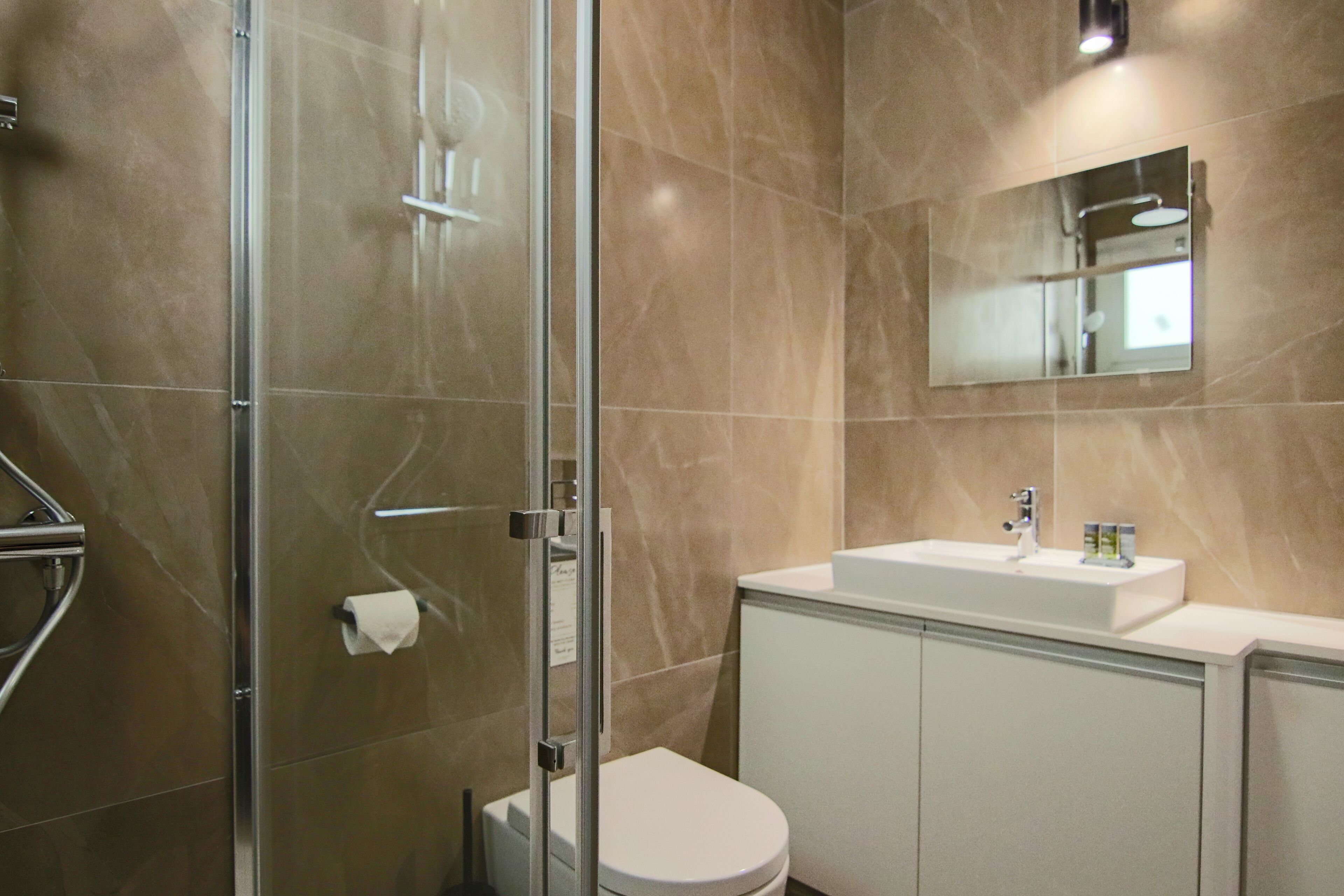 Een moderne badkamer met een douchecabine van glas, een wit toilet en een wastafel met spiegel erboven.