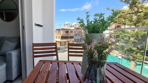 A balcony with a grey sofa, wooden chairs, a table, and a potted plant. - Phaedrus Living: Seaside Luxury Flat Athina 123 (Paphos)