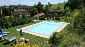 Une piscine entourée de pelouse et d’arbres, avec des chaises longues et des parasols.