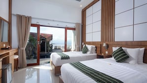 Quarto de hotel com duas camas, cabeceira de madeira, uma escrivaninha e vista para o mar.