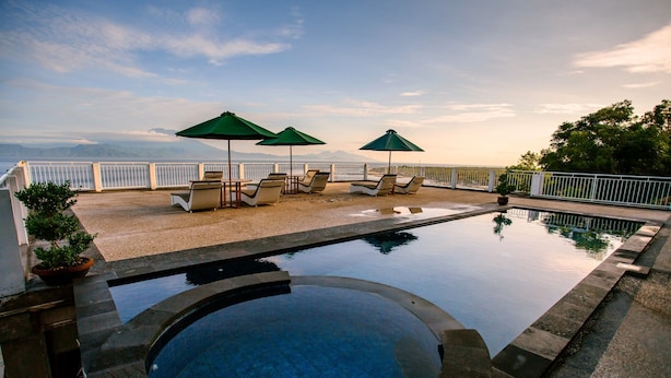 Uma piscina com cadeiras de descanso e guarda-sóis, cercada por uma cerca branca e com vista para as montanhas.