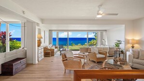 A spacious living area with a view of the ocean, furnished with wicker chairs and a glass coffee table. - Mahina Kai, Princeville Oceanfront Luxury, Steps to Hideaways (Princeville)