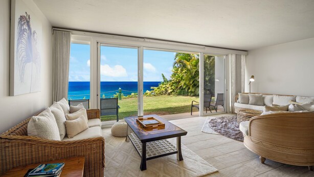 A spacious living room with a view of the ocean, a wicker sofa, a coffee table, and a wicker armchair. - Mahina Kai, Princeville Oceanfront Luxury, Steps to Hideaways (Princeville)