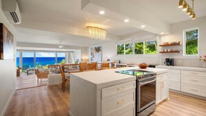 A modern kitchen with white cabinetry, a central island, and a view of the ocean. - Mahina Kai, Princeville Oceanfront Luxury, Steps to Hideaways (Princeville)