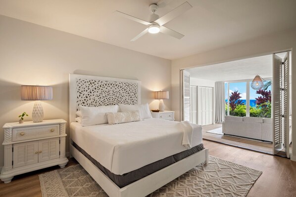 A bedroom with a large bed, two bedside tables with lamps, a ceiling fan, and a view of the outdoors through a sliding door.