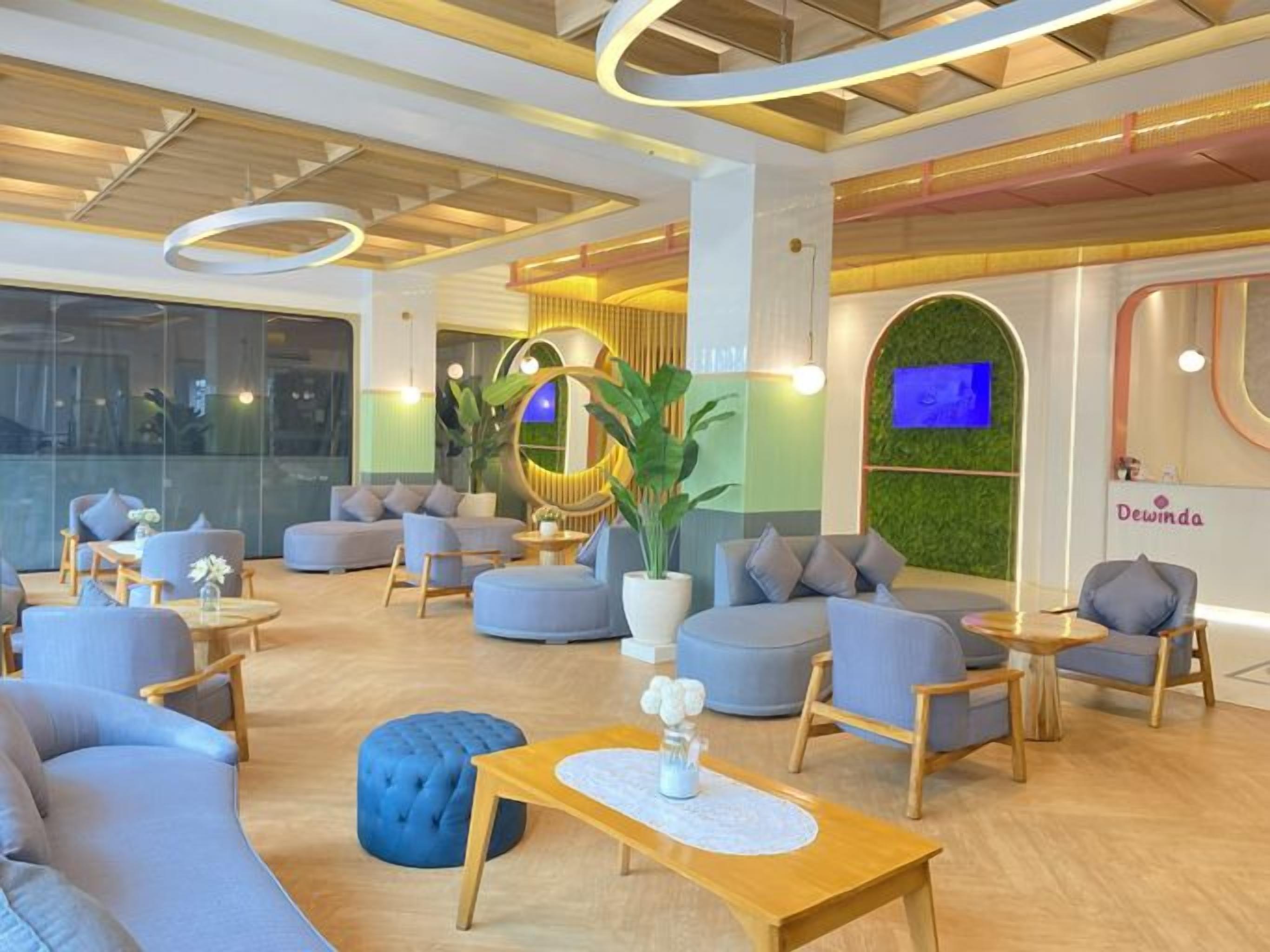 Un hall d’hôtel moderne, avec des canapés, des fauteuils, une table basse et une grande plante en pot.