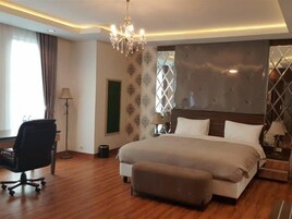 A hotel room with a large bed, a desk, a chair, and a chandelier.