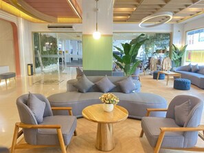 A modern lounge area with a large sectional sofa, two armchairs, a round wooden coffee table, and a potted plant.