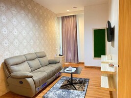 A living room with a sofa, a small table, a flat-screen TV, and a green chalkboard on the wall.