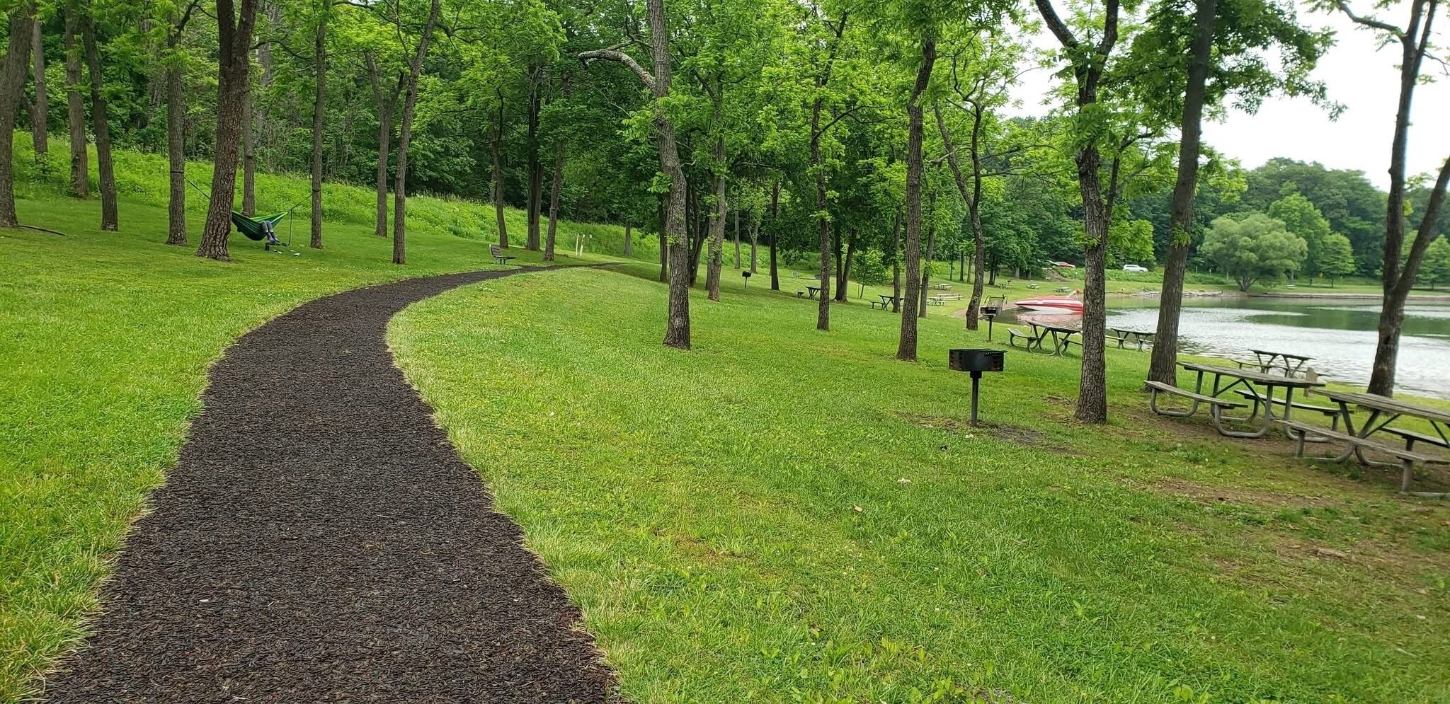 Un parque con un sendero sinuoso, mesas de picnic y bancos.