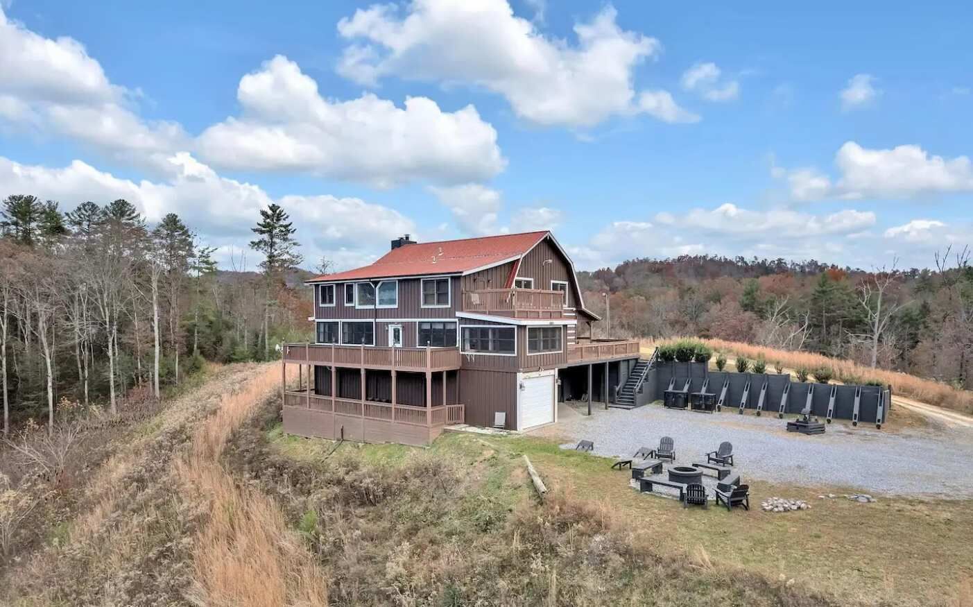 Une cabane à deux étages dotée d’une grande terrasse, d’un espace salon extérieur et d’un garage.