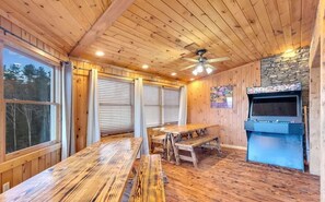 A wooden interior with a table and benches, a stone fireplace, and a ceiling fan.