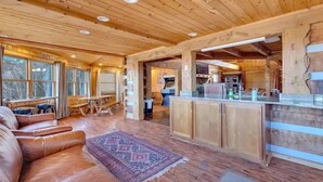 A cozy cabin interior with a wooden ceiling, a dining area, a kitchen, and a seating area with a rug. - 5,000 Sq Ft 5BR/4.5BA Cabin, 20Min to Pigeon Forge (Sevierville)