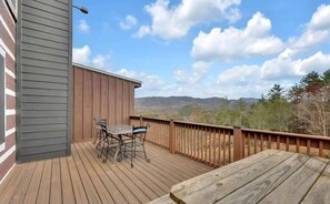 A wooden deck with a table and chairs, overlooking a mountainous landscape.