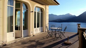 Une terrasse en bois avec une table et des chaises, donnant sur un lac et offrant une vue sur des montagnes en arrière-plan.