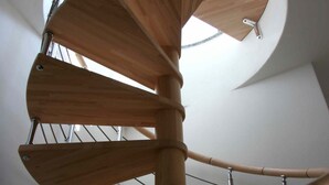 Un escalier en colimaçon avec des marches en bois et une rampe en métal, menant à une lucarne circulaire.