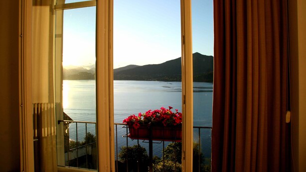 Une vue depuis une fenêtre, avec un panier de fleurs sur le balcon, donnant sur un lac paisible et des montagnes lointaines.
