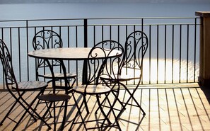 A wooden deck with a round table and four chairs, surrounded by a metal railing. - Appartamento Panorama (Ghiffa)