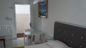 A hotel room with a bed, a desk, and a chair. There is a painting on the wall and a door leading to the outside. - Quiet and comfortable room in the center. B&B (Santo Domingo)