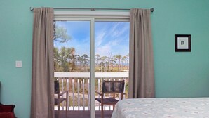 Una habitación con cama, una silla y vistas a un espacio exterior con terraza y sillas.
