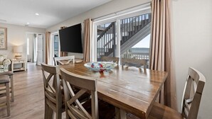 Un comedor con una mesa de madera, sillas, un televisor y vistas a una escalera que conduce a un balcón.