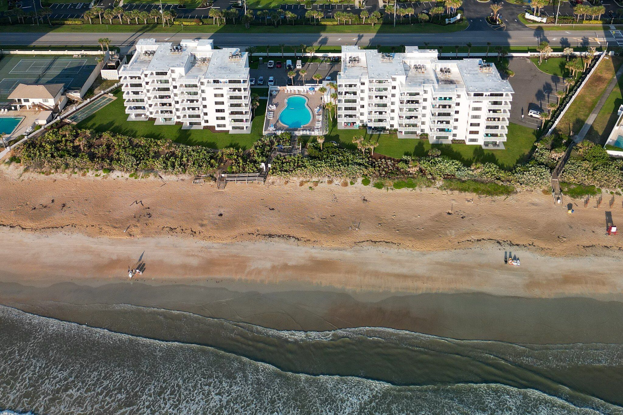 A beachfront hotel with multiple floors, a swimming pool, and a beach in the foreground.