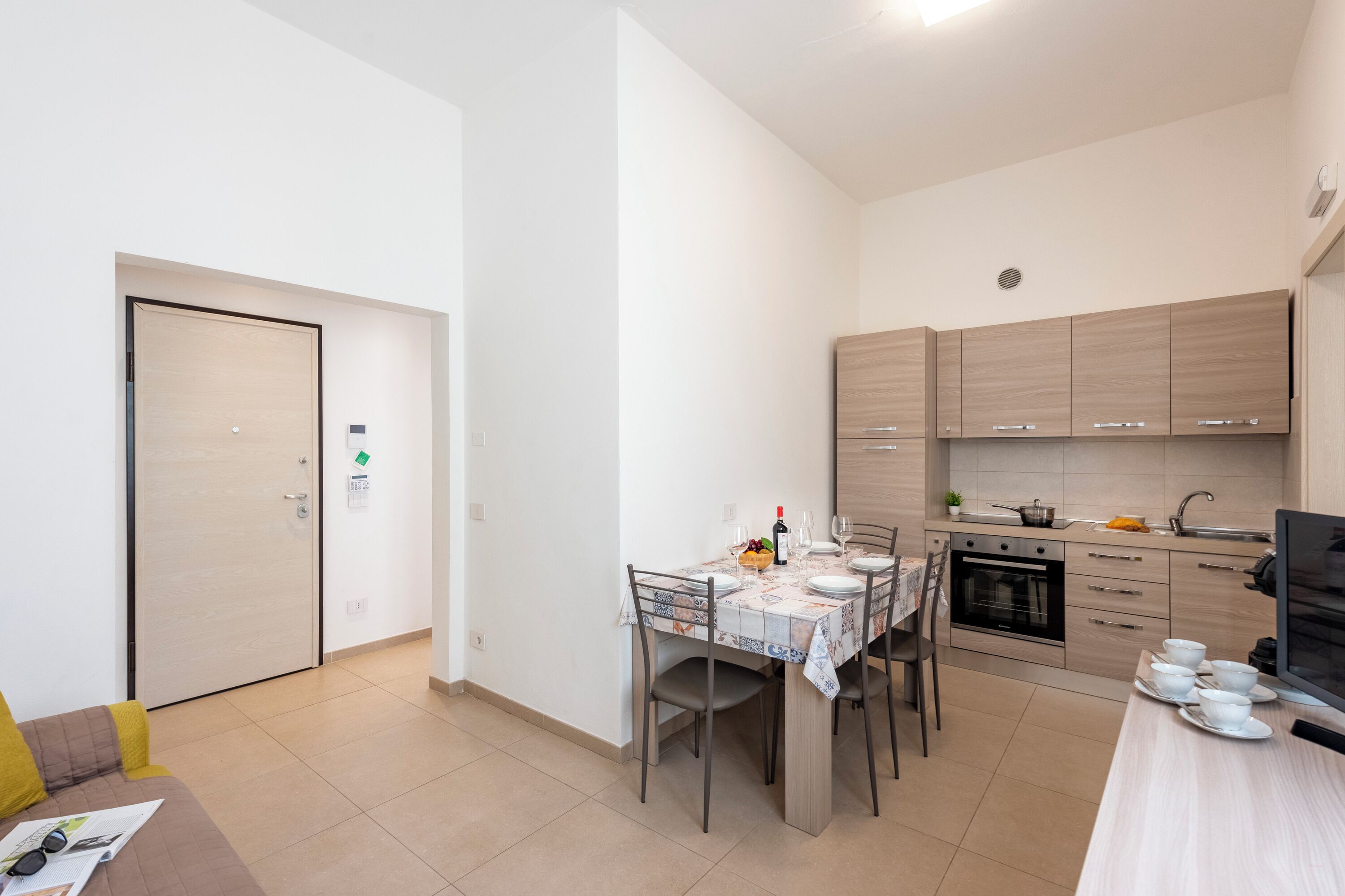 A modern kitchen with a dining area, featuring a built-in oven, a sink, and a flat-screen TV.