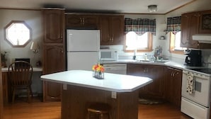 Une cuisine avec des meubles de rangement en bois, un îlot central, un réfrigérateur, un four à micro-ondes et un four traditionnel.