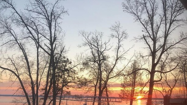 Un paysage enneigé avec un coucher de soleil, des arbres et une clôture.