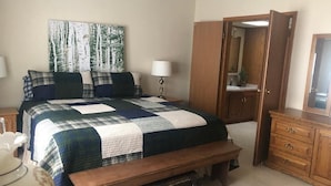 Une chambre à coucher avec un grand lit, un banc en bois, une commode, un miroir et un tableau accroché au mur.