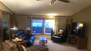 Un salon comprenant un canapé, un fauteuil et un pouf, une télévision et un ventilateur de plafond.