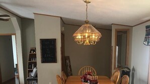 Une salle à manger avec une table et des chaises en bois, un lustre et une pancarte « Bienvenue » accrochée au mur.