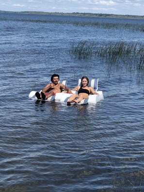 Deux personnes se détendent sur un bateau dans un lac paisible, avec une côte visible au loin.