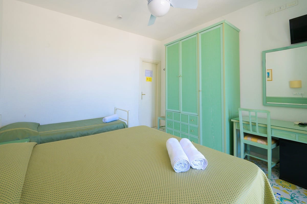 A room with two beds, a green wardrobe, a desk with a chair, and a mirror.