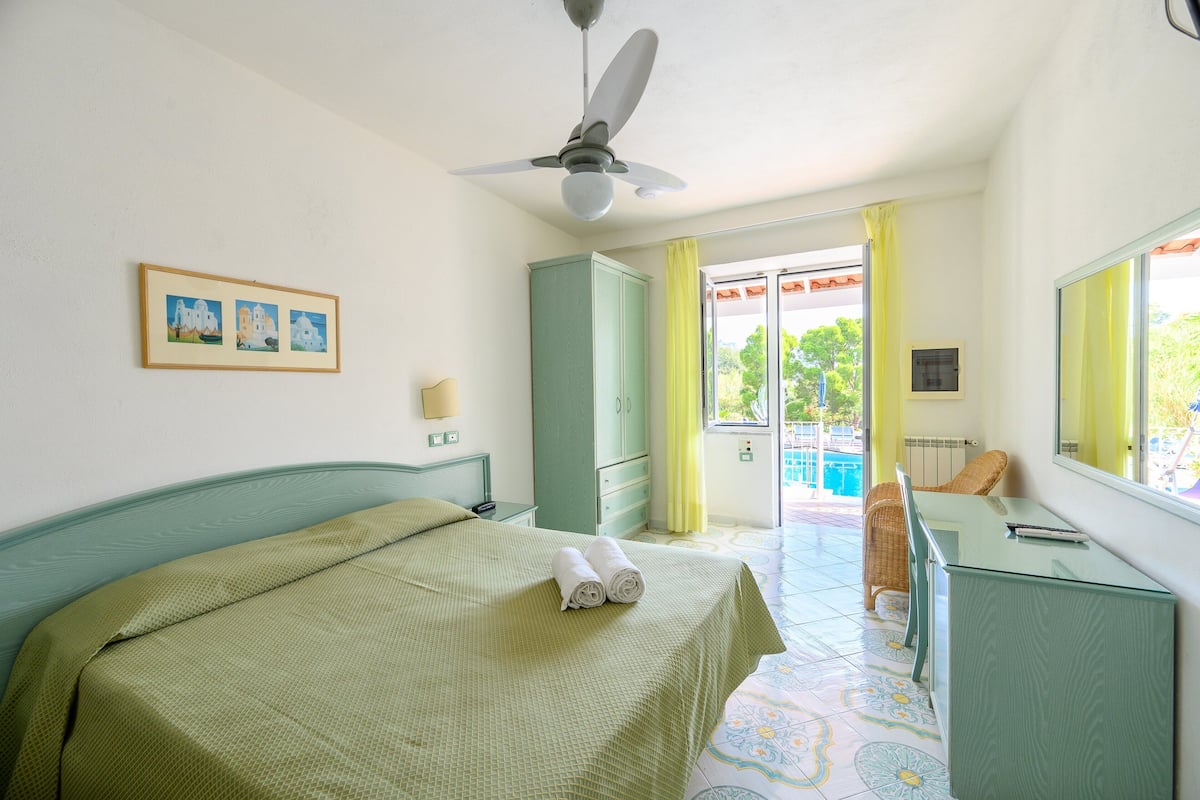 A bedroom with a bed, a desk, a chair, a wardrobe, and a ceiling fan.