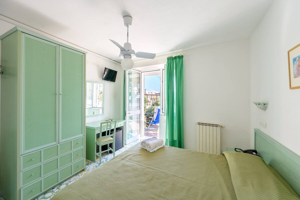A room with a bed, a desk, a wardrobe, and a ceiling fan.